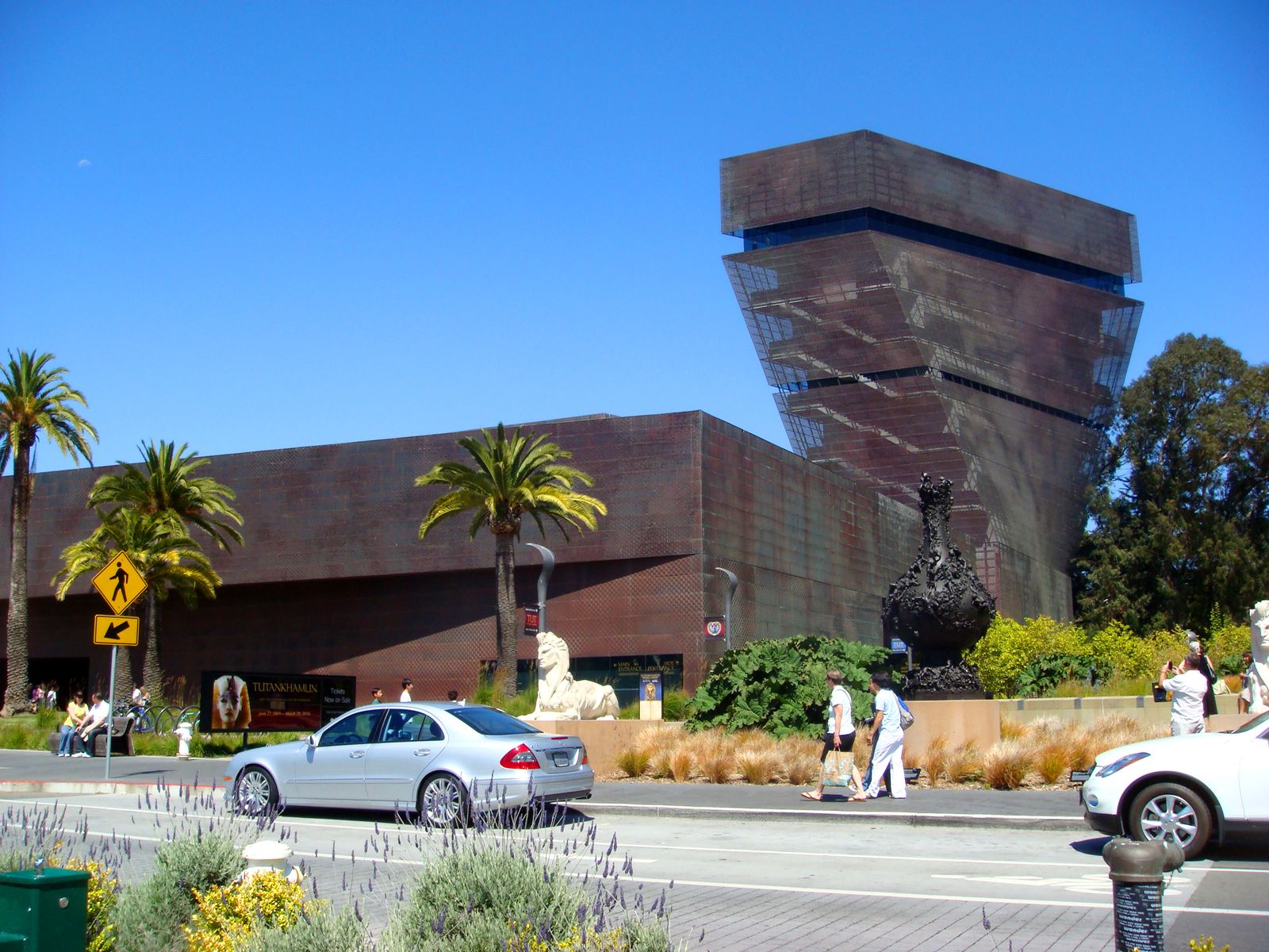 The museum's copper-clad tower above low buildings with palm trees and a street in front.