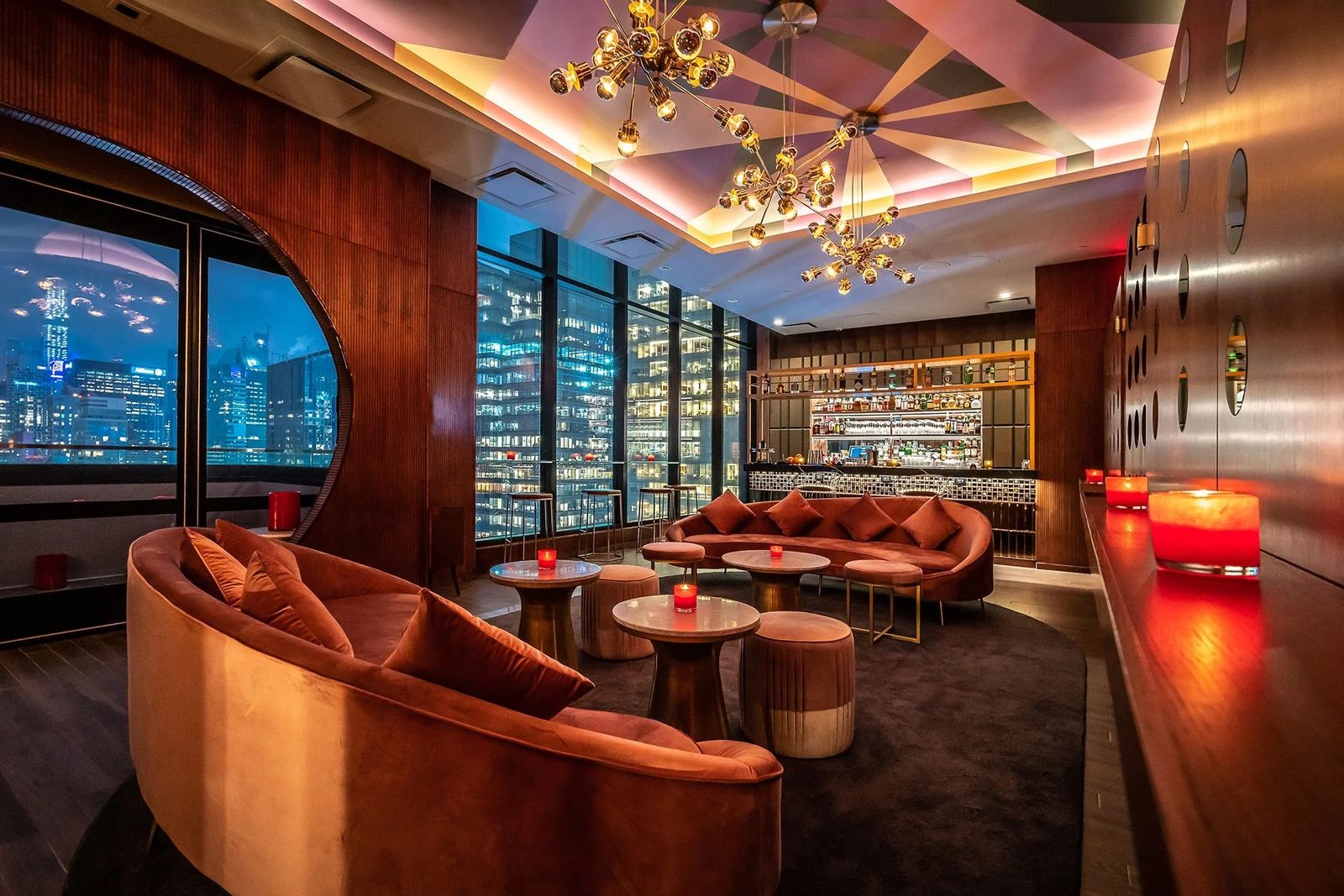 A lounge with curved velvet seating and tall windows over the city at night