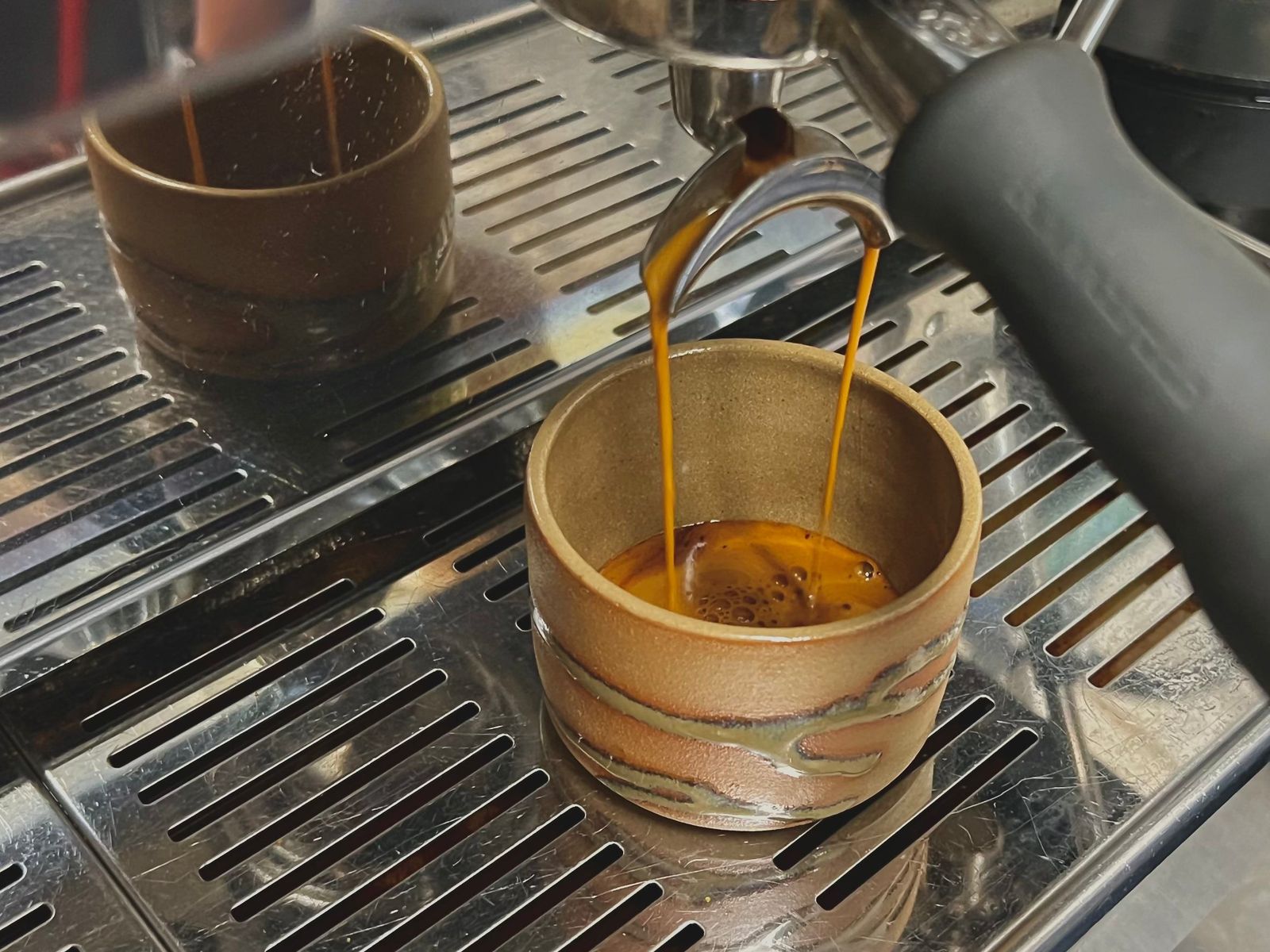 Espresso pouring from a portafilter spout into a small gold-rimmed cup on a drip tray.