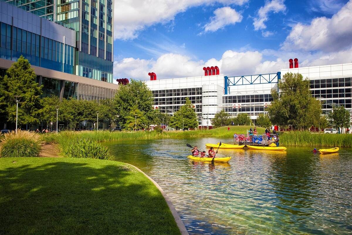 Kayaks on the lake at Discovery Green with a green lawn and city buildings behind