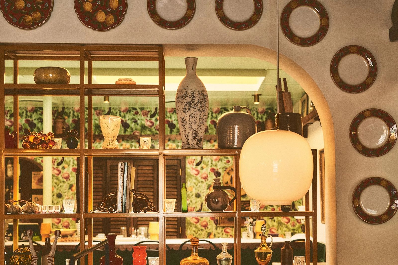 Interior shelving with ceramics and vases under an arched opening framed by round wall details