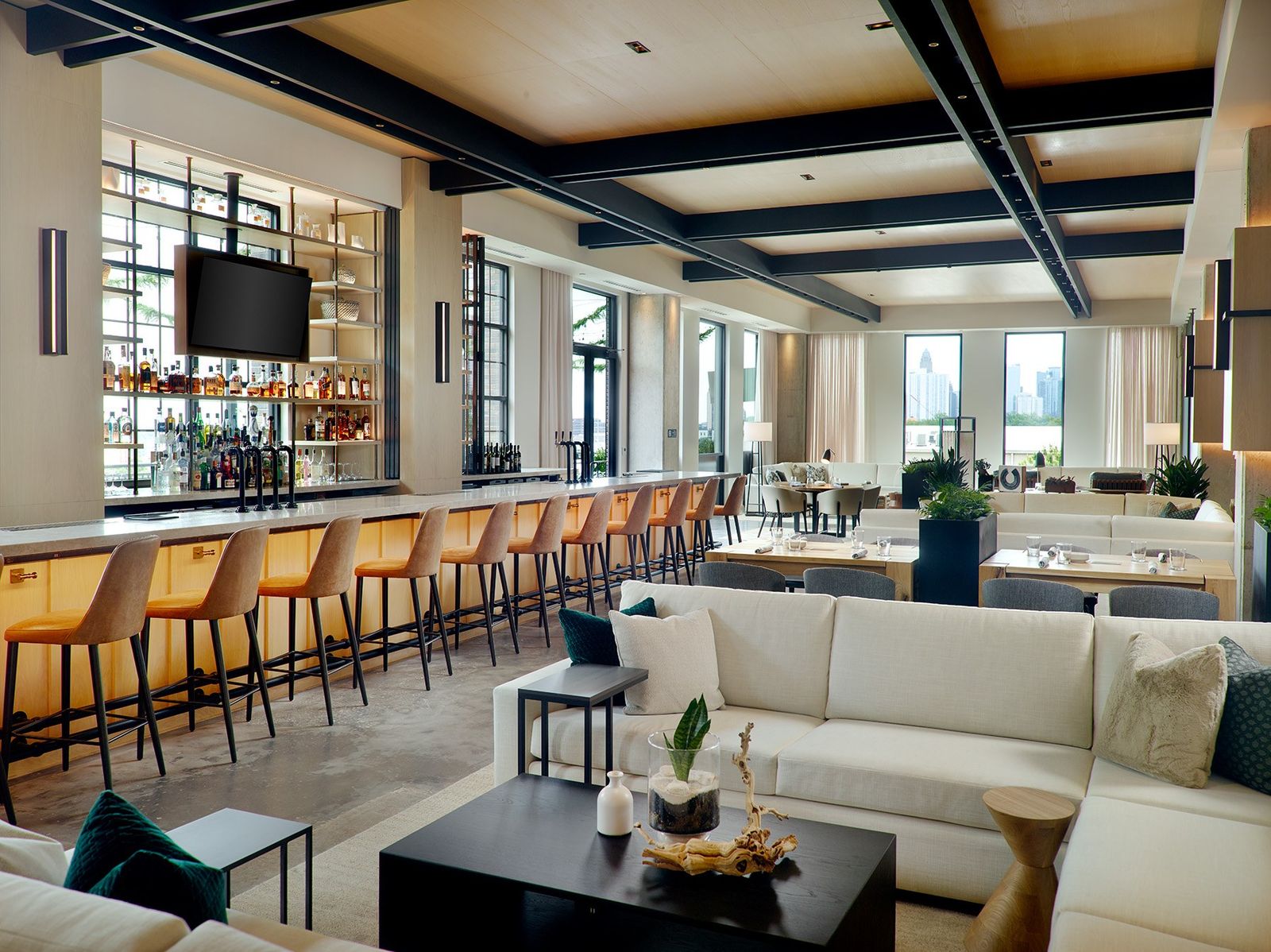 A bright bar and lounge with a long counter, tall windows, beamed ceiling and cream sofas