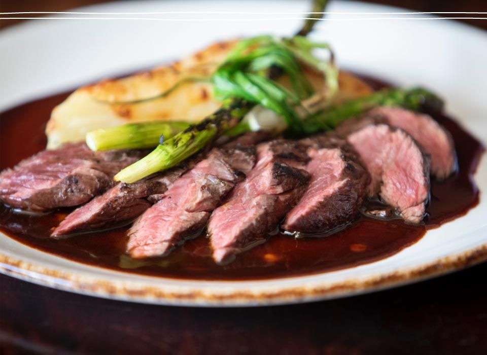 Sliced beef with asparagus over a dark sauce on a wide white plate.