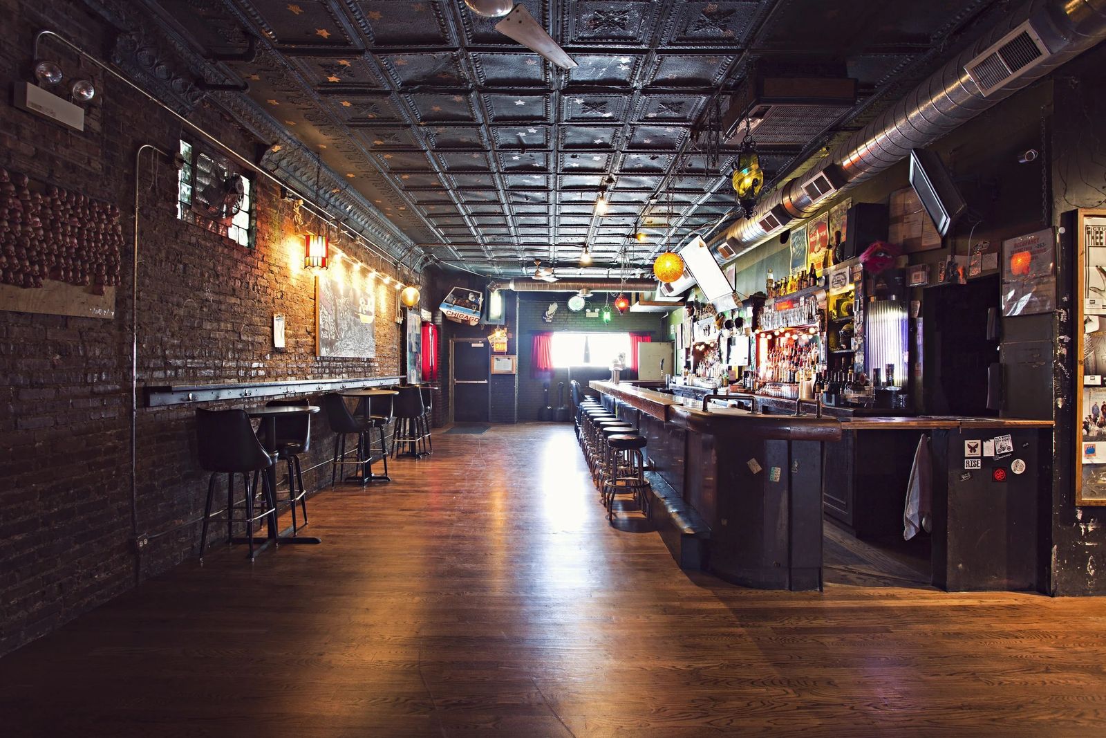 A long dark bar room with a wood floor, brick walls and a bar along the left.