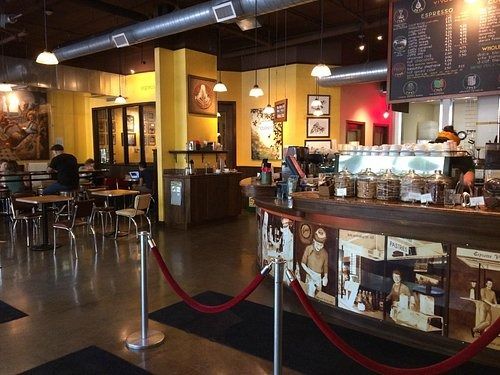 A cafe with yellow walls, pendant lights and a counter lined with glass jars, with a rope barrier in the foreground.