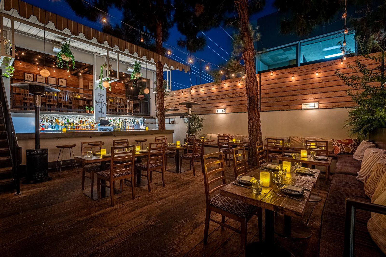 Fia's patio at night with string lights, wooden tables and a glowing bar in the background
