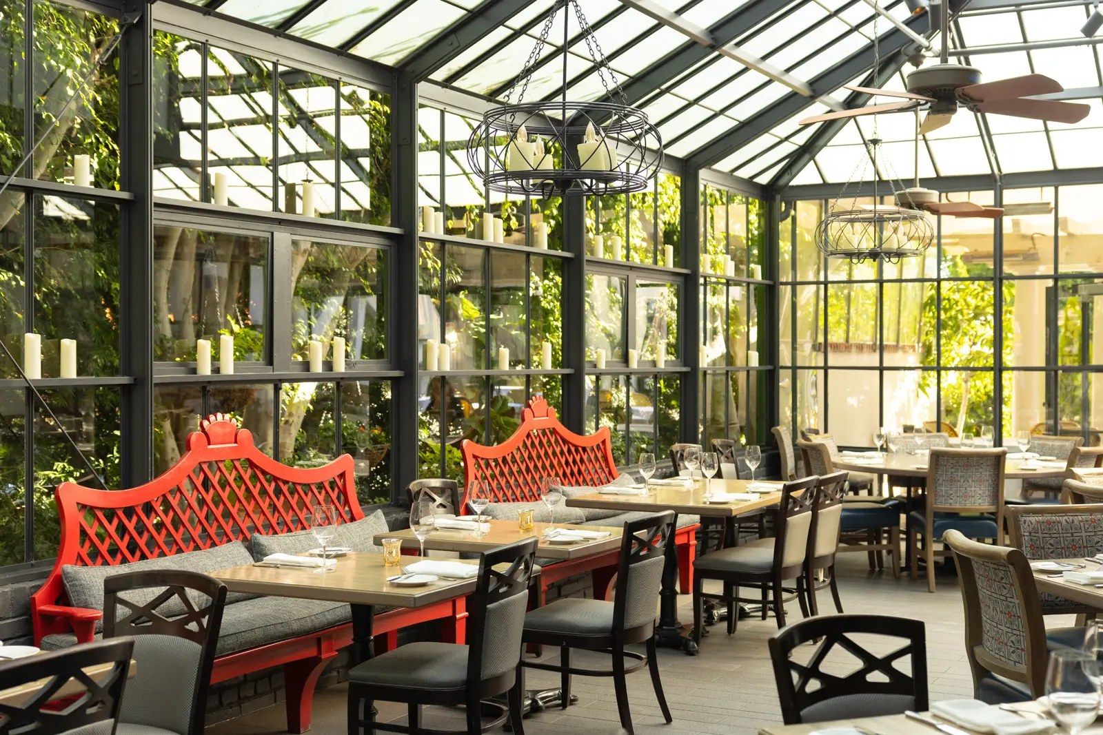 A glass-walled conservatory dining room with plants and red banquettes.