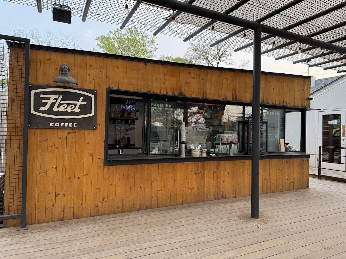 A wooden coffee building with a service window and a Fleet Coffee sign, beside a covered patio deck.