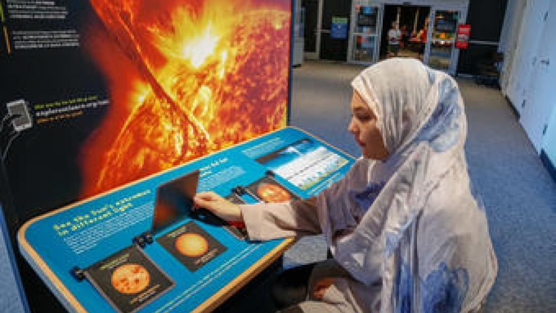 A visitor at an interactive exhibit display with a glowing solar image behind her.