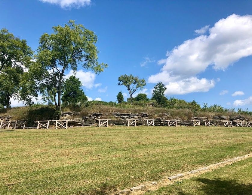 Grassy hillside with a low stone and timber fort wall and trees under a blue sky