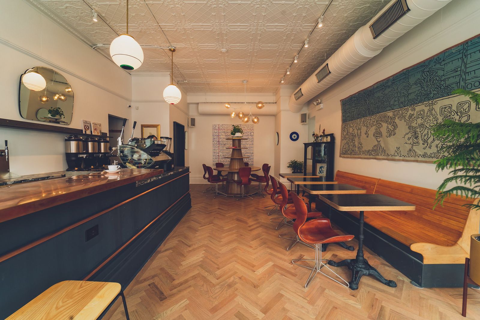 A bright cafe with a long dark counter, wood floors, red chairs and globe pendant lights.