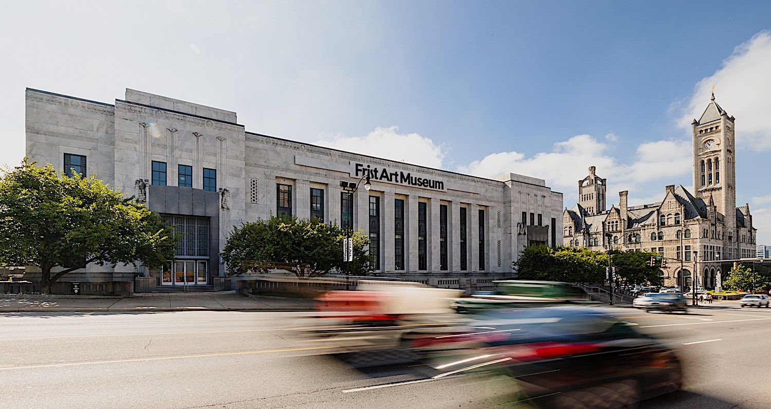 Exterior of the Frist Art Museum's Art Deco building on a street with a blurred passing car
