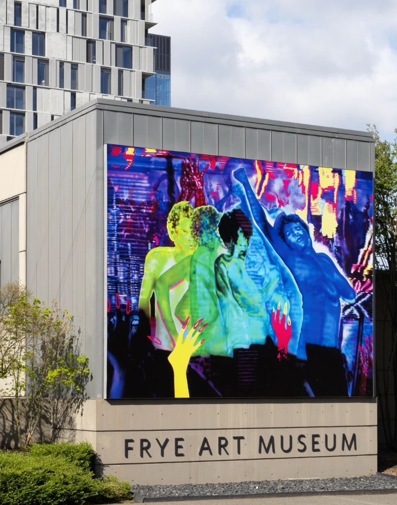 A gray building with a large colorful illuminated artwork above a concrete sign reading Frye Art Museum, with a tall tower behind it.