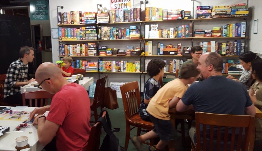 Players seated at tables in front of shelves stacked with board games