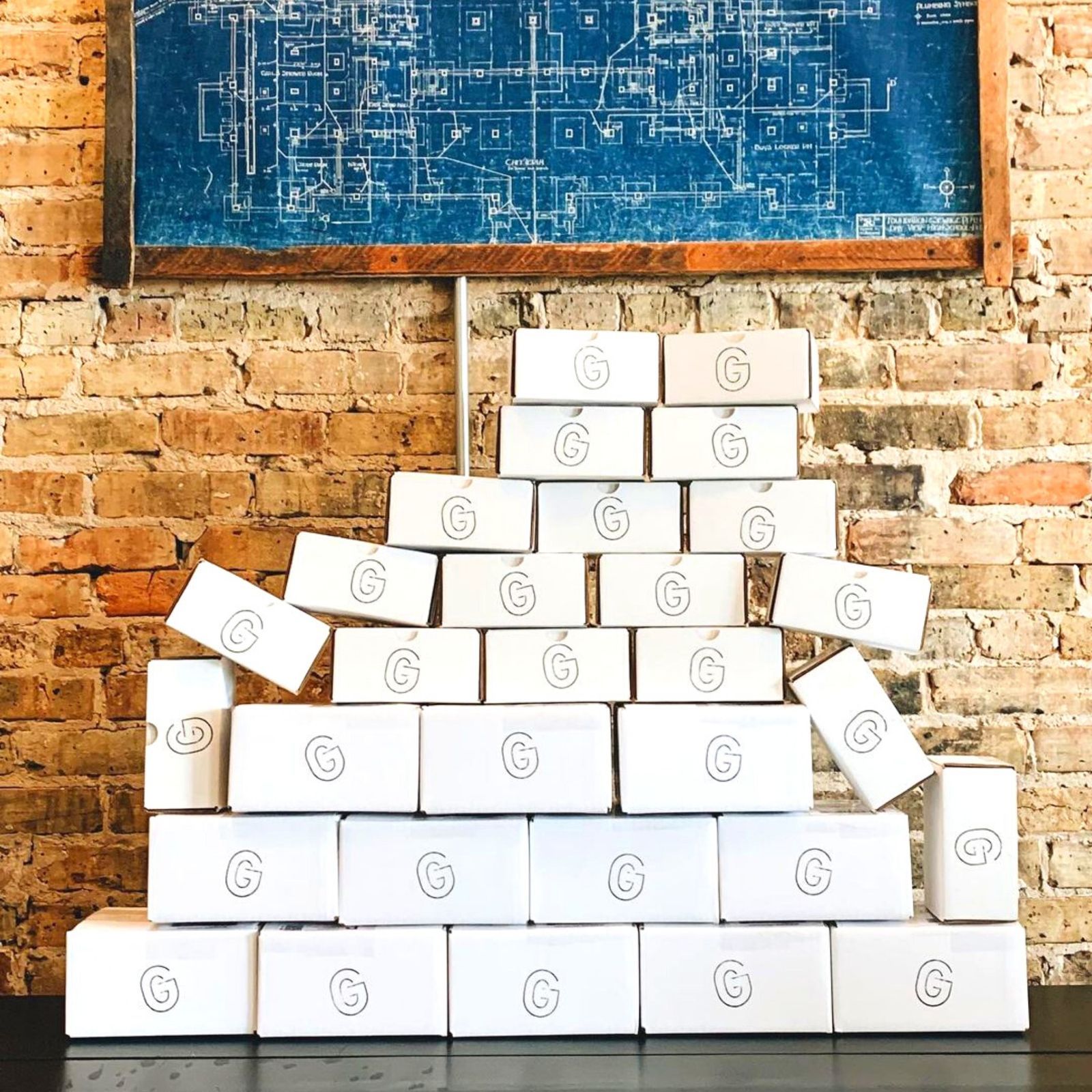 A brick wall with a blueprint-style print above a stack of white boxes marked with a G logo.