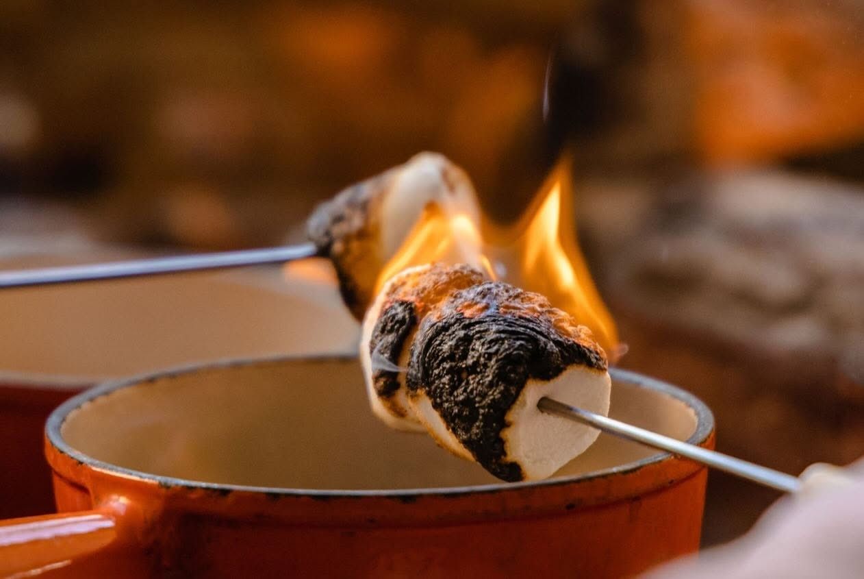 A marshmallow on a long fork catching fire over a copper fondue pot.