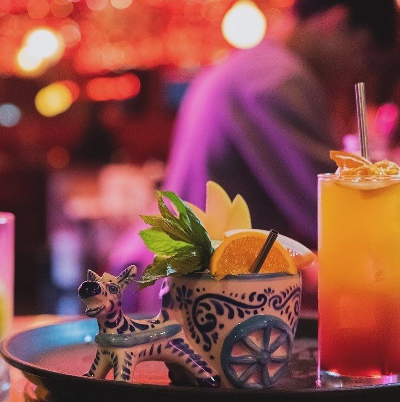 Two cocktails on a tray, one in a ceramic donkey-cart mug garnished with citrus and mint