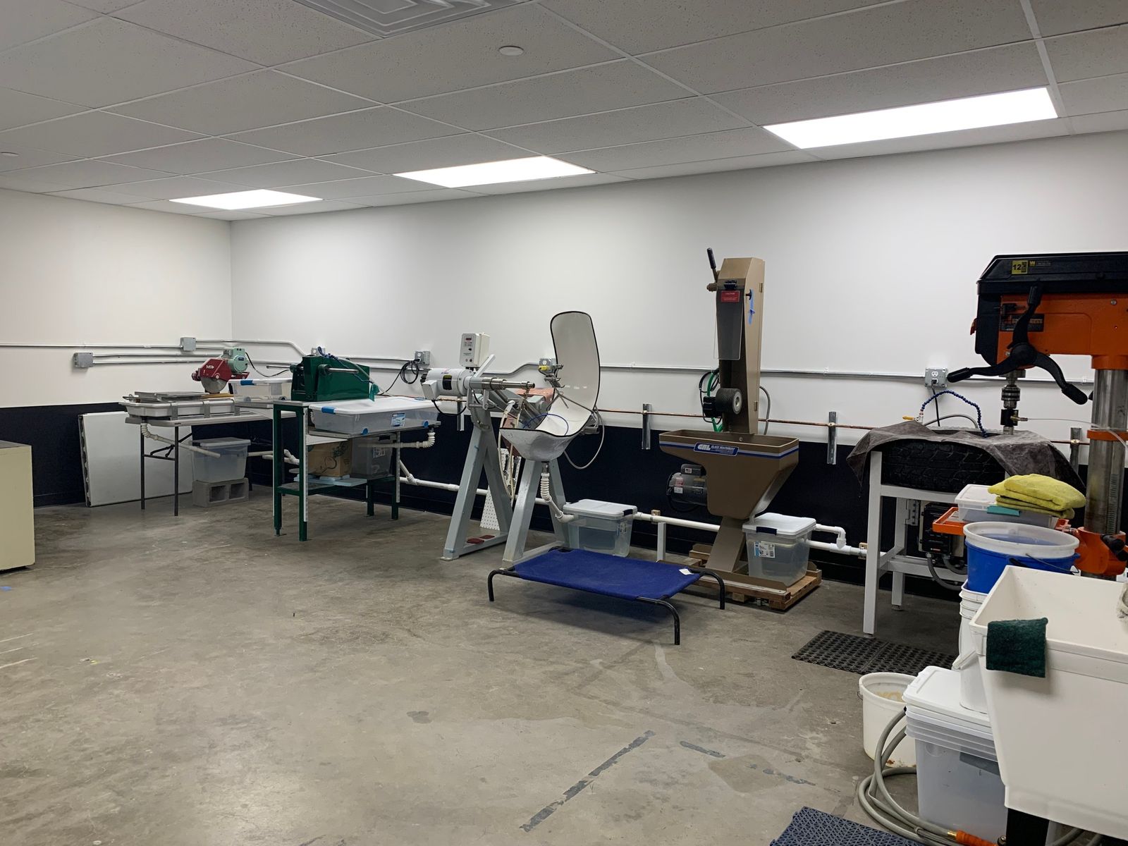 A bright studio workshop with workbenches, tools and grinding equipment under fluorescent lights.
