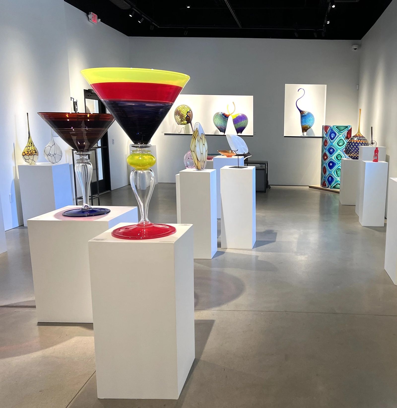 Gallery room with colorful blown glass vessels on white pedestals