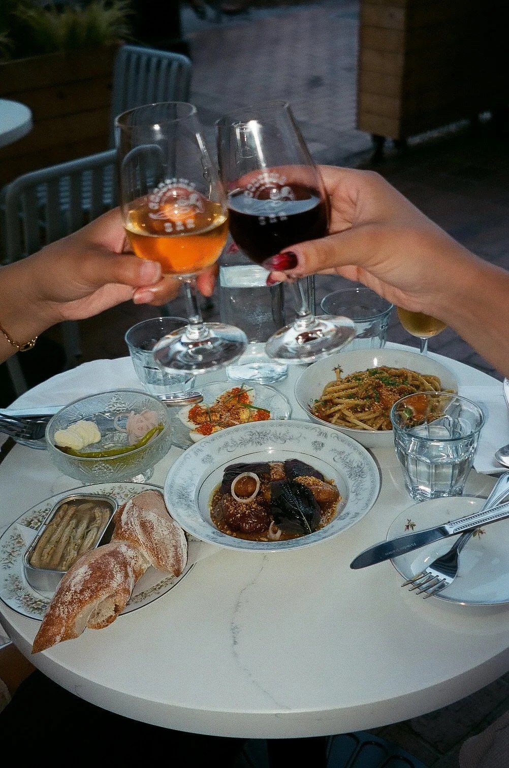 Two wine glasses clinking over a table of shared plates