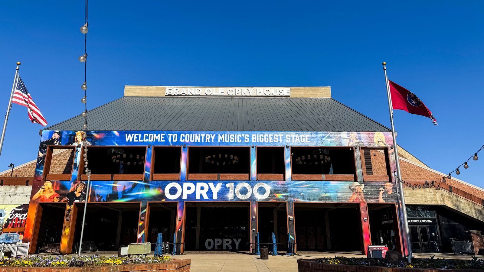 Exterior entrance of the Grand Ole Opry House with flags and a banner reading Opry 100