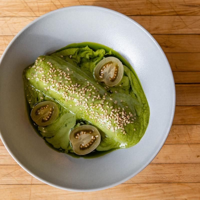 Green puree with sesame seeds and small tomatoes in a gray bowl on a wooden board