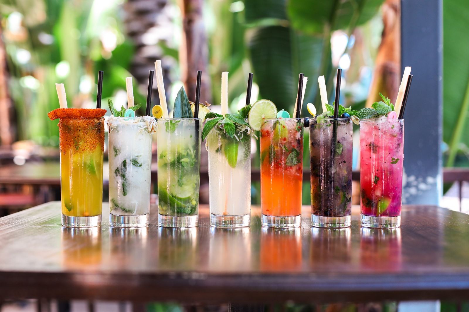 A lineup of mojito-style cocktails in tall glasses with mint and lime on a wooden table.