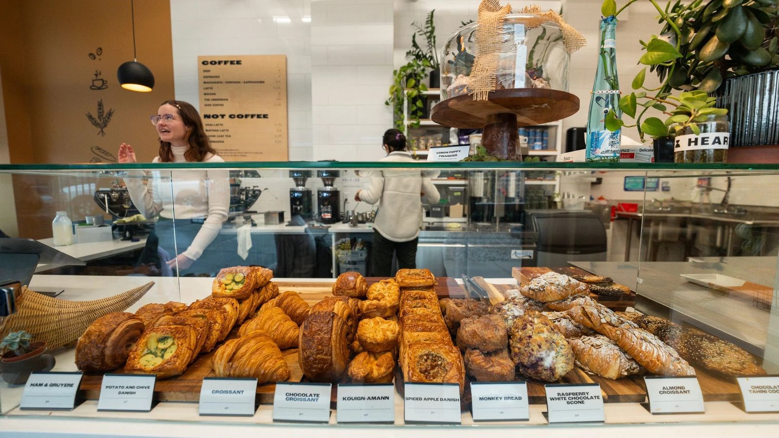 A glass pastry case with trays of croissants and pastries and a staff member behind the counter.