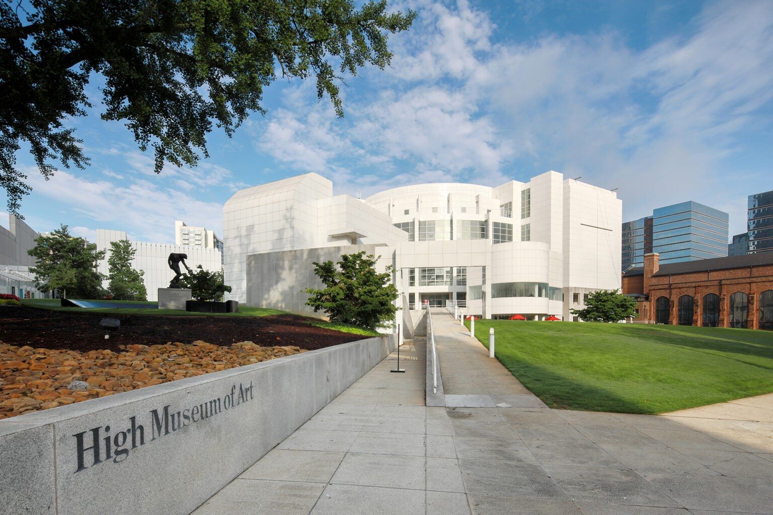 The white High Museum of Art building seen from a walkway, with the museum's name on a low wall in the foreground