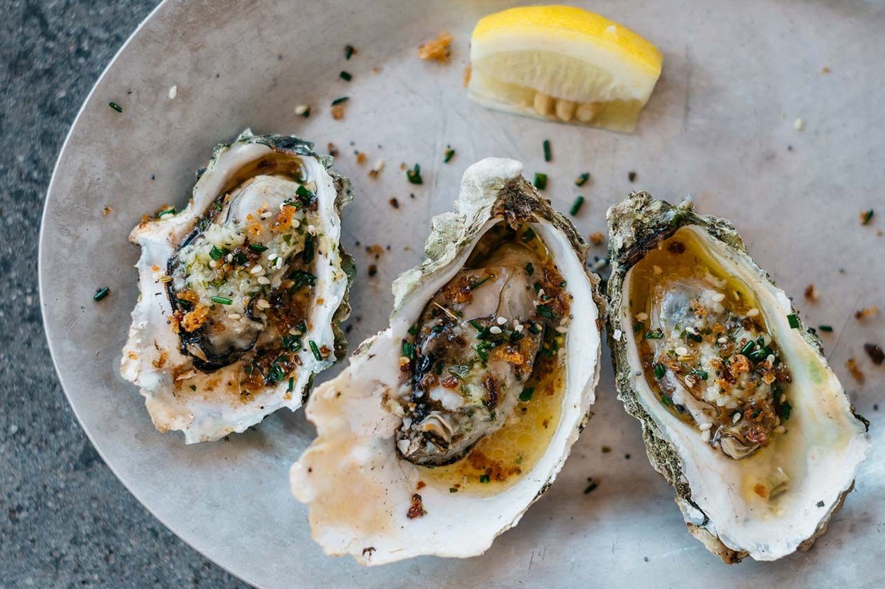 Three baked oysters with toppings on a round plate with a lemon wedge