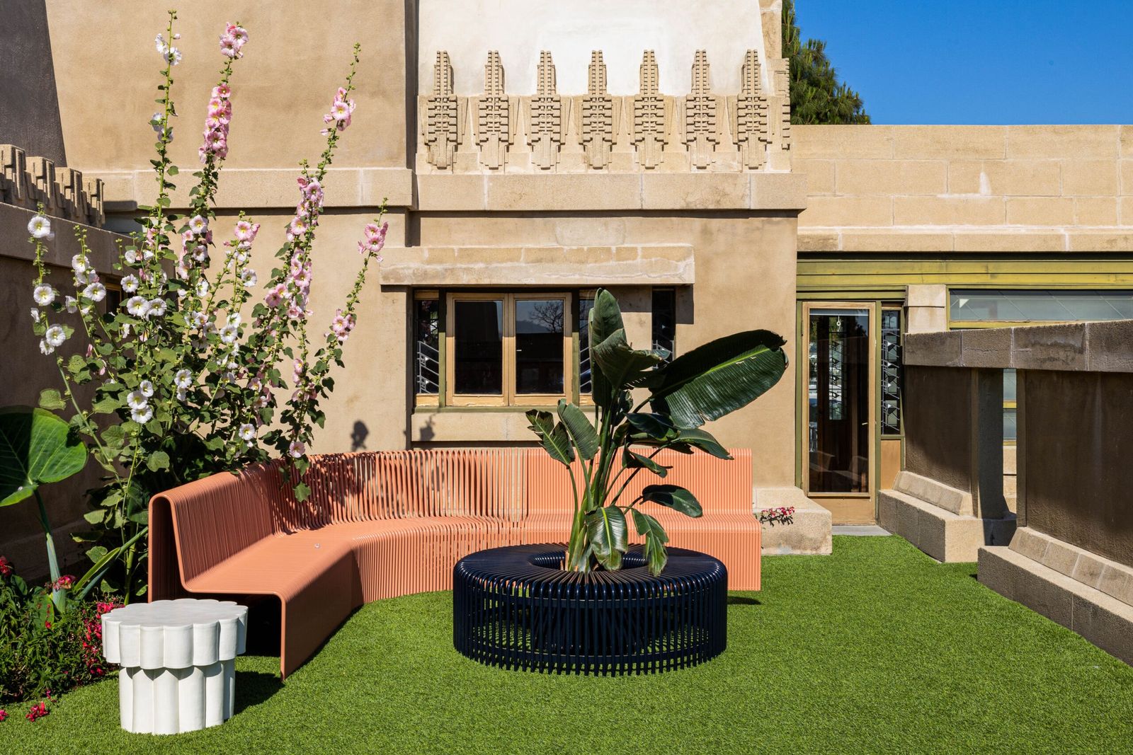 A terrace of the stepped stone house with an outdoor sofa, plants and a lawn in front.