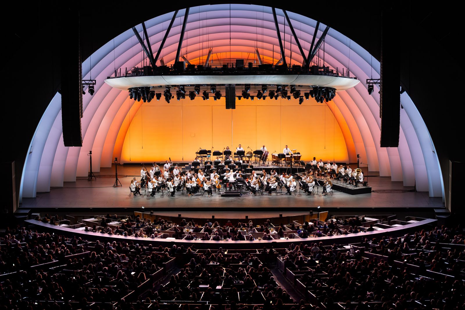 The Hollywood Bowl's white shell stage lit orange with an orchestra seated beneath it.