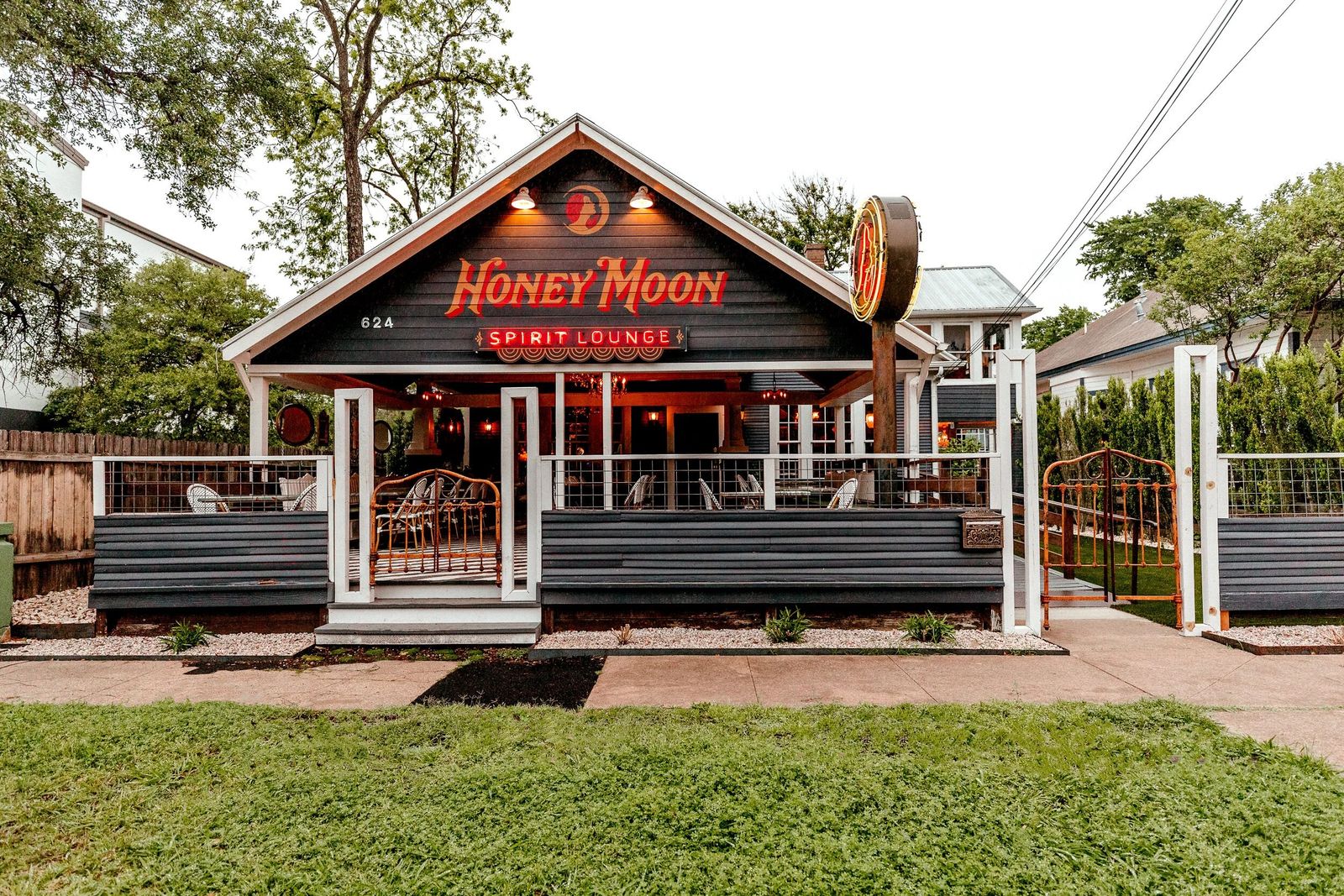 A small wooden house-style bar with a lit Honey Moon sign, a porch and a lawn in front.