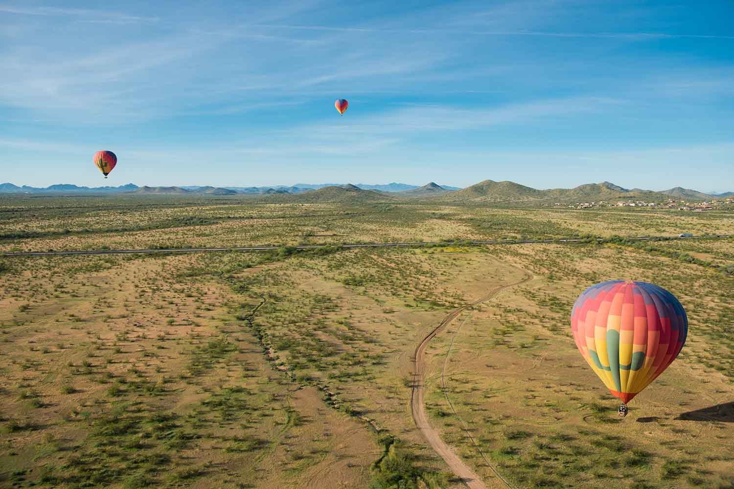 A hot air balloon over green desert landscape with a dirt track and mountains