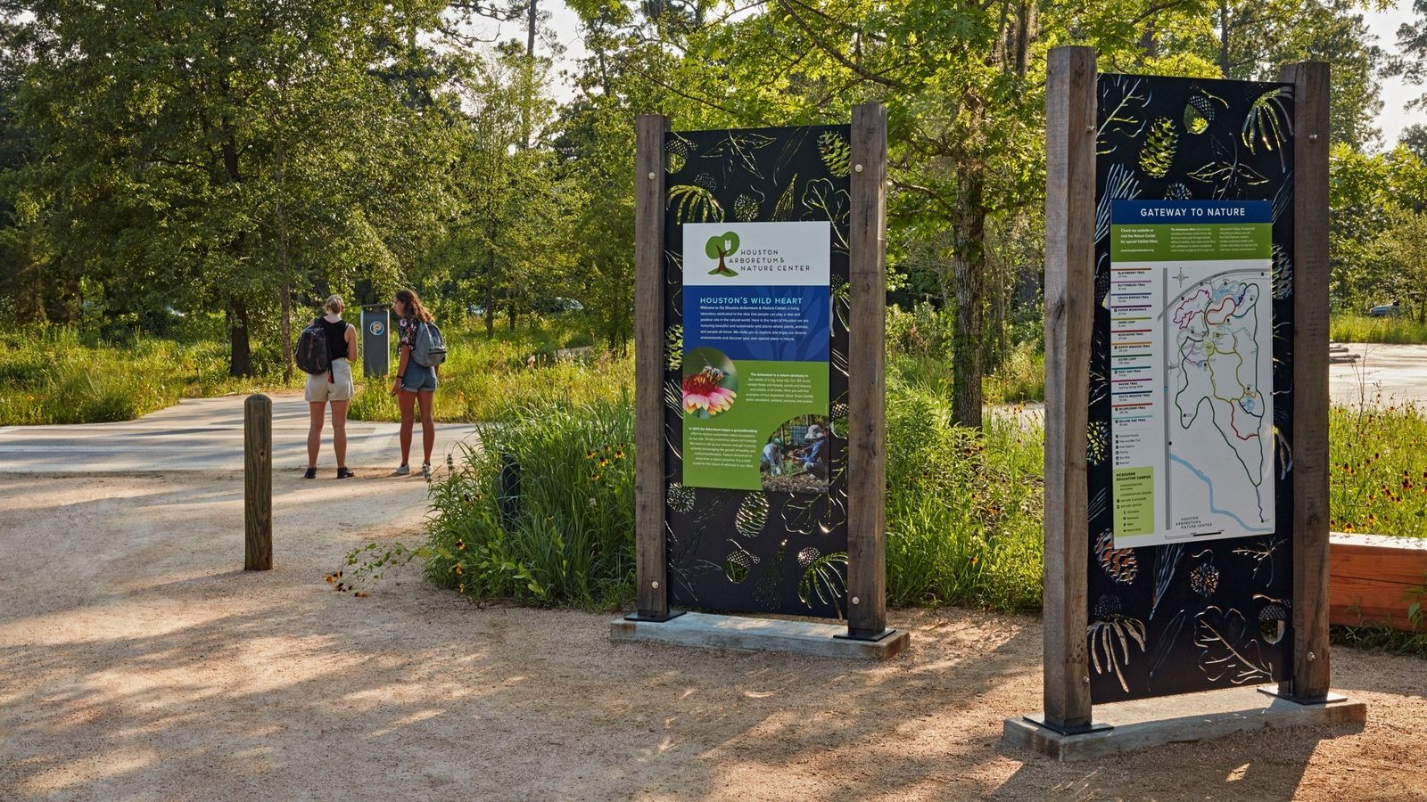 Two trail information signs beside a wooded path with a few visitors in the distance