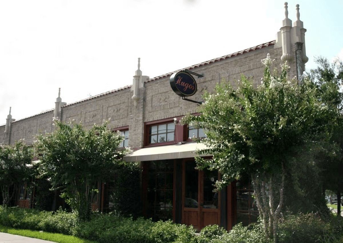 Stone building exterior with trees and a hedge in front, Hugo's restaurant