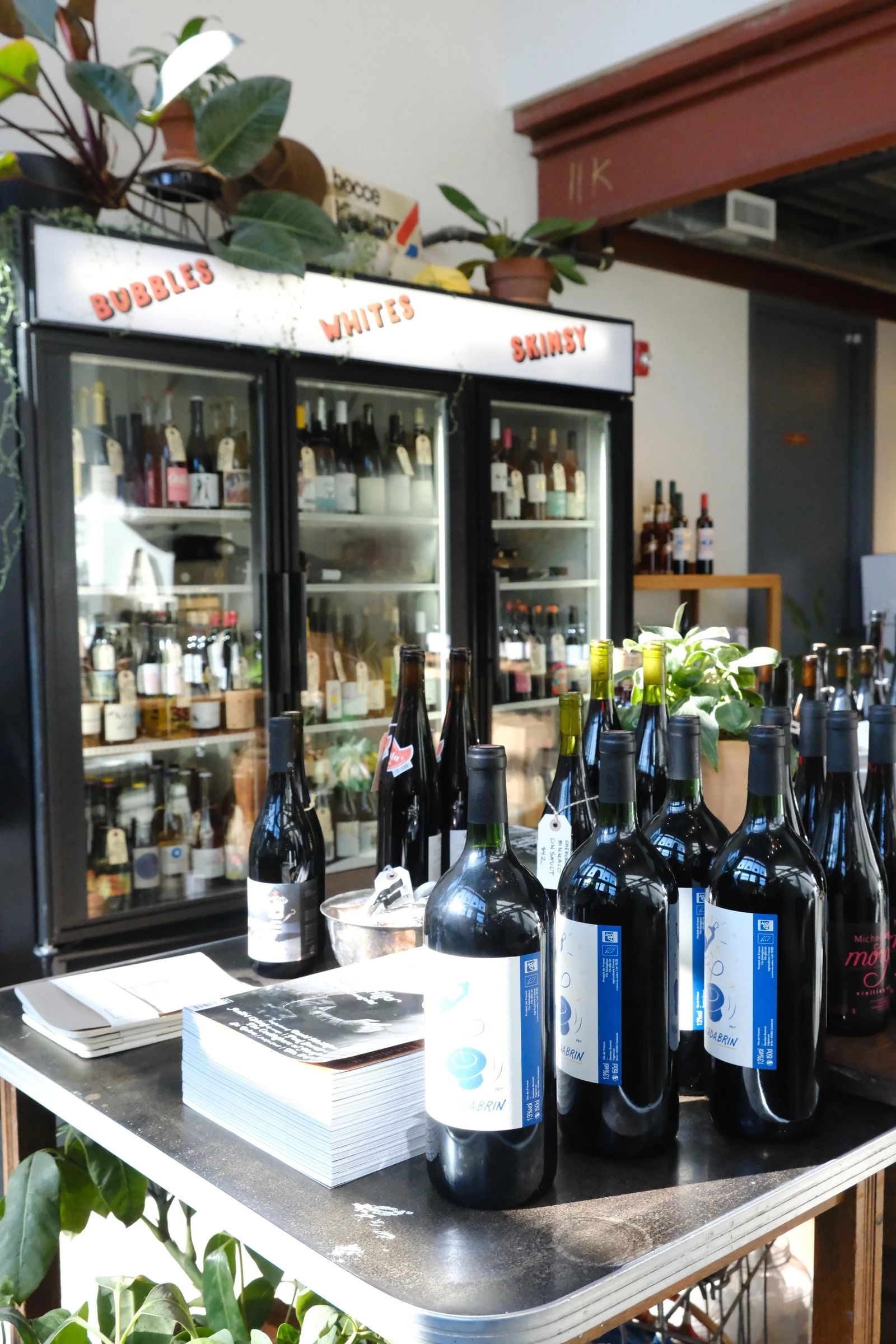 A glass-door refrigerator filled with wine bottles beside a counter stacked with books.