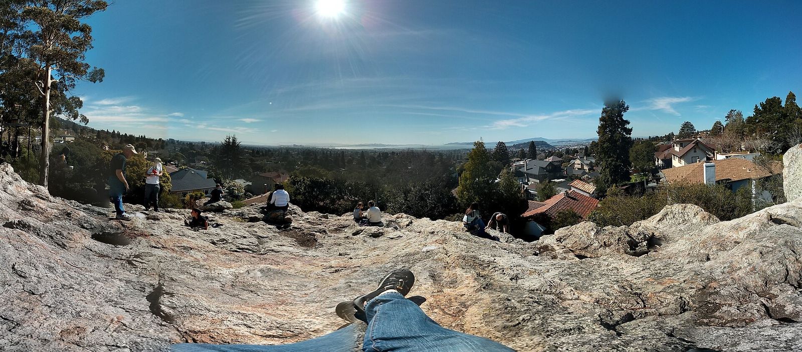 A wide view from a granite outcrop over rooftops and trees toward the bay, with a few people on the rock.