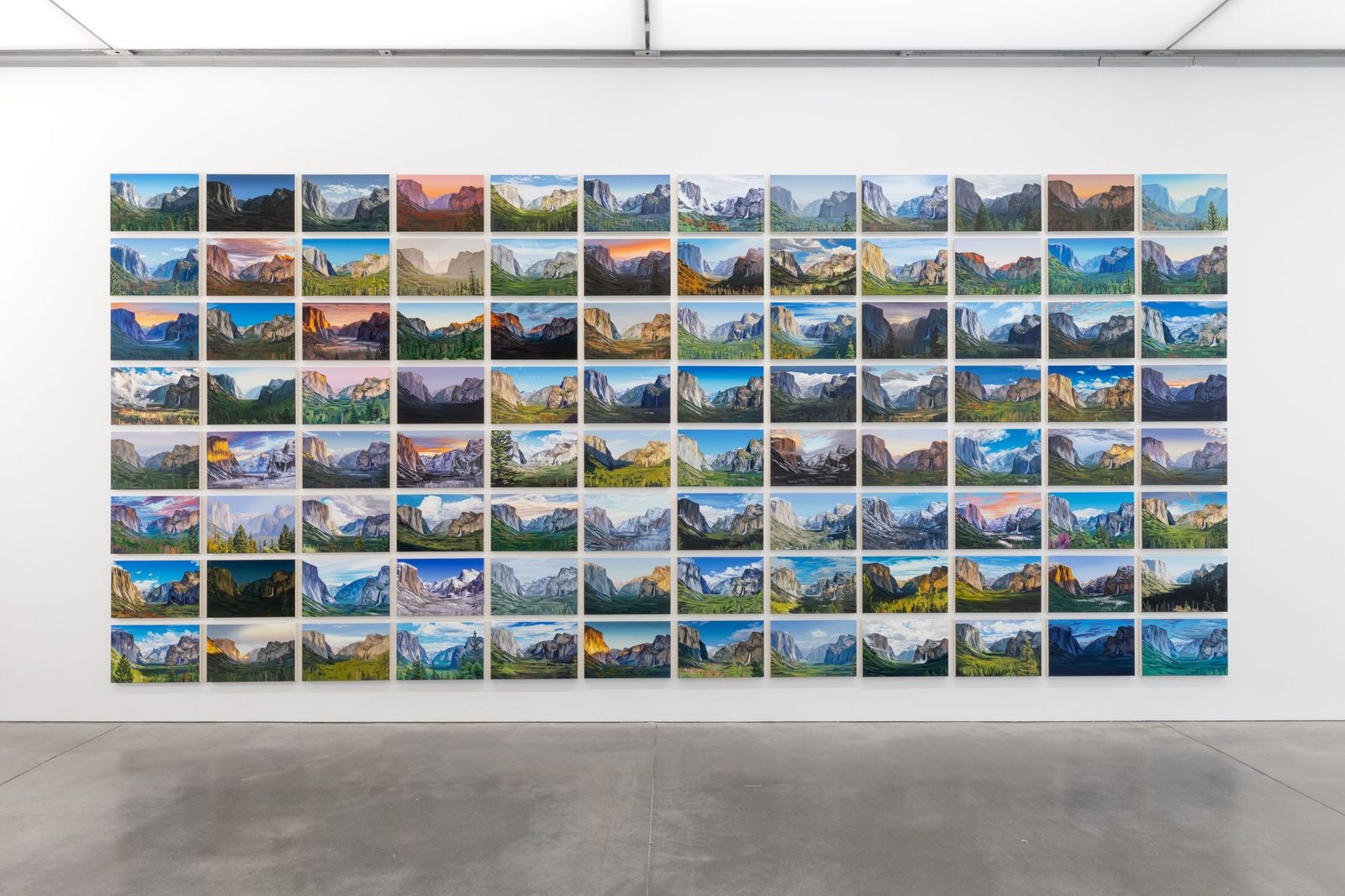 Large grid of small landscape paintings hung on a white gallery wall