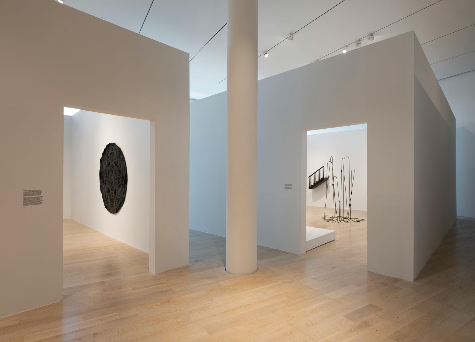 Empty white gallery rooms with a round black artwork on one wall and a column