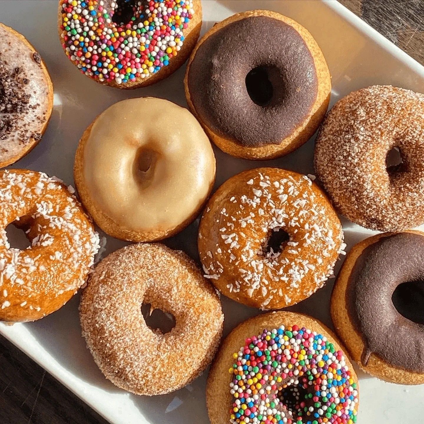 A plate of glazed, sprinkled and powdered donuts.
