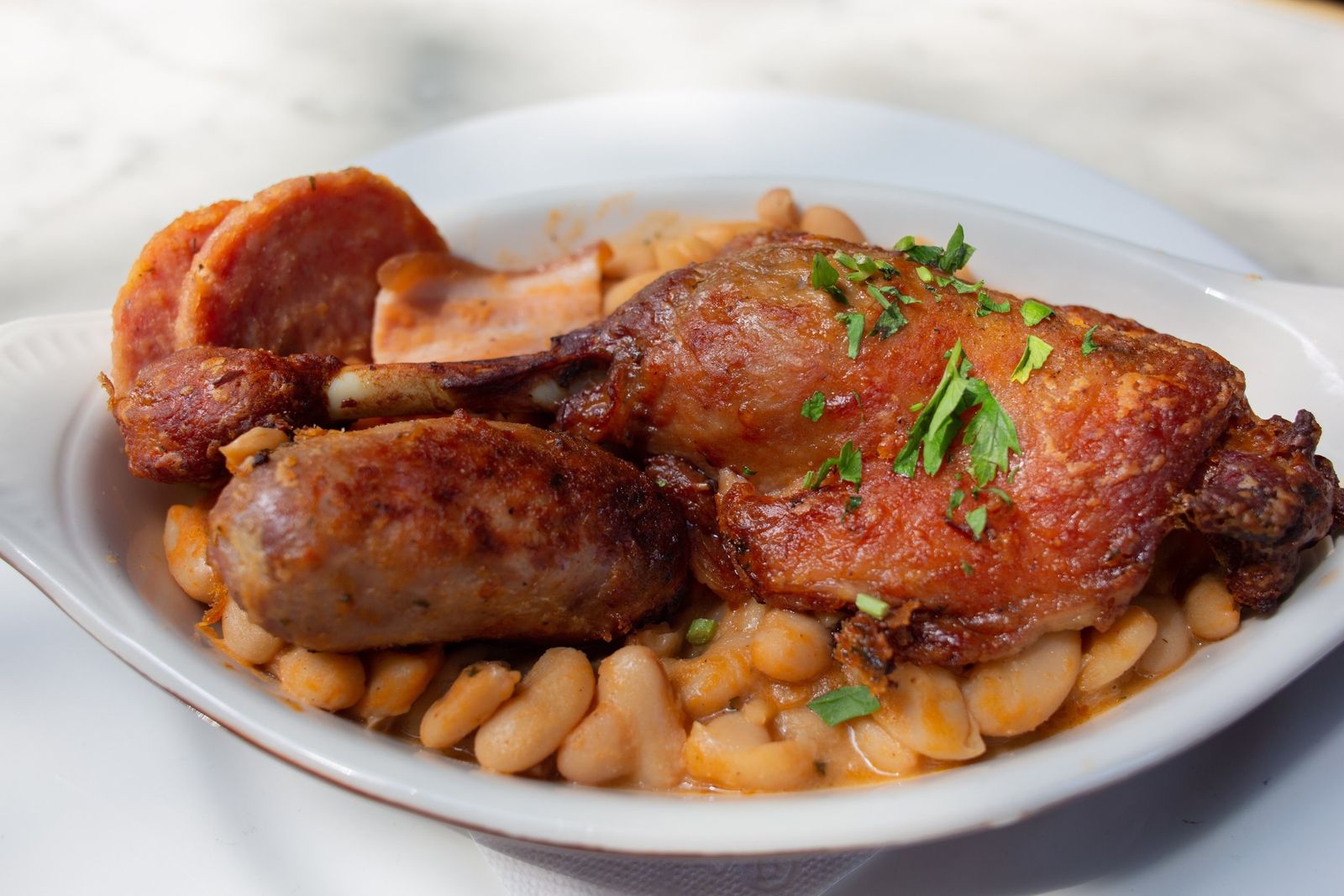 A bowl of sausage and roasted chicken over white beans