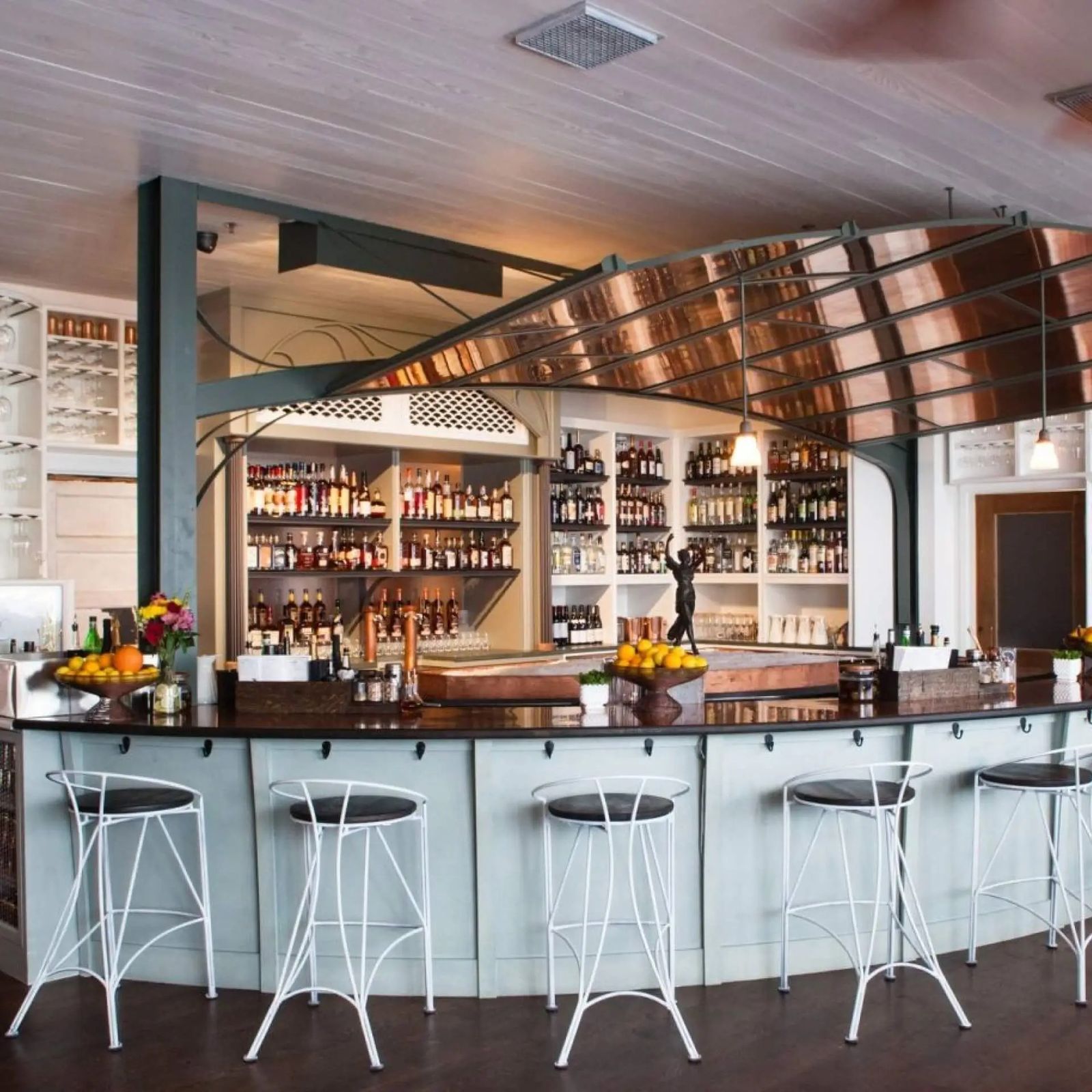Curved bar with white stools and lit shelves of bottles under a copper-toned ceiling