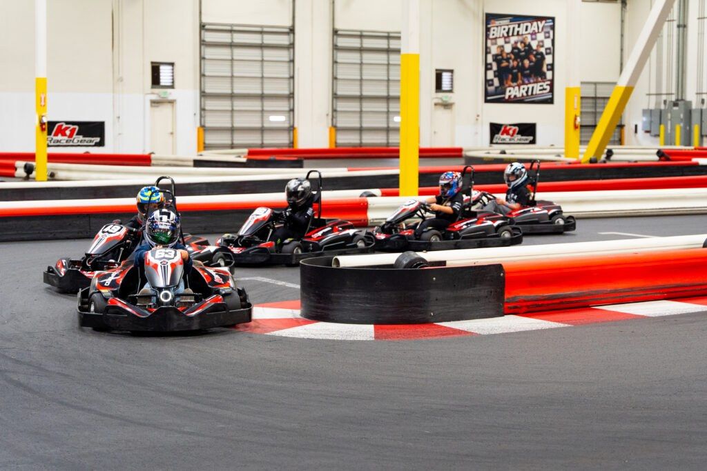 Several go-karts racing around a red-and-white barrier on an indoor track.