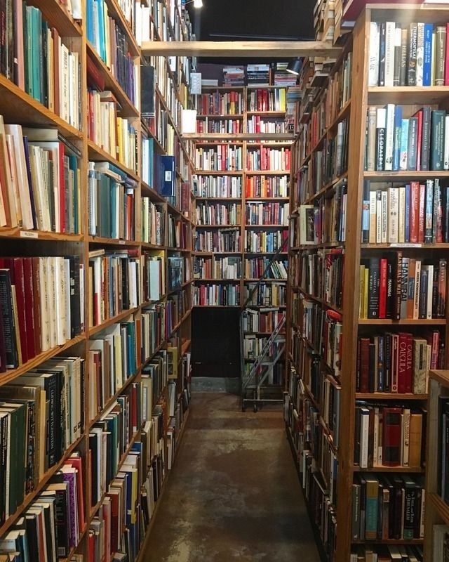 A narrow aisle between tall wooden shelves packed with books