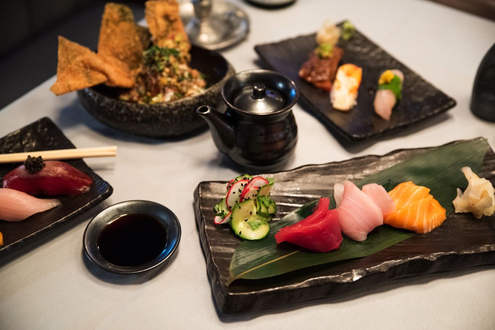 A spread of sashimi, rolls and small dishes on dark plates and a green leaf.