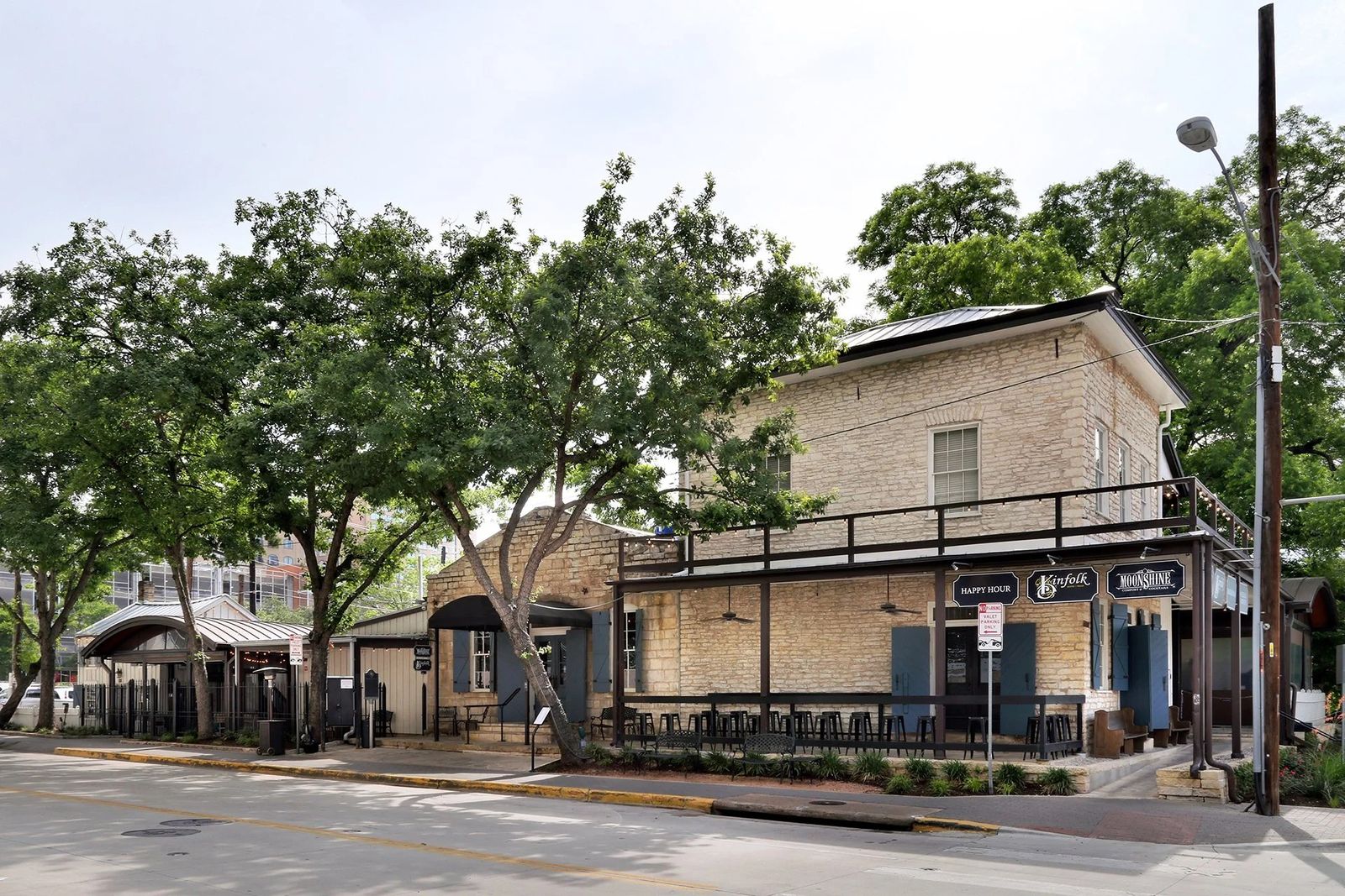 A two-story stone building with a porch under trees on a street corner.