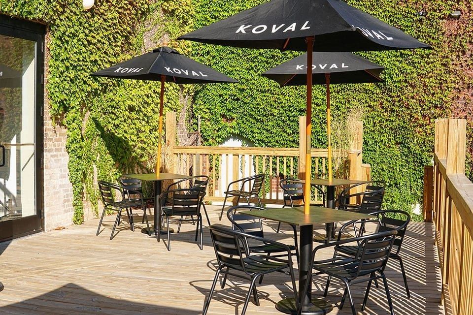 A deck with black umbrellas and tables beside an ivy-covered wall.
