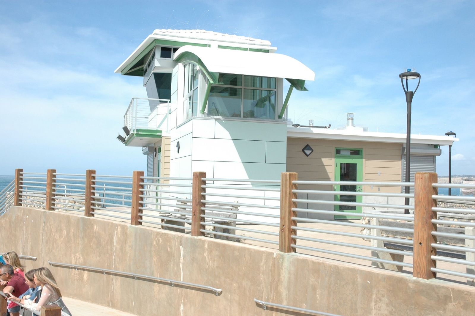 A white lifeguard tower with a green-trimmed roof above a seawall with a railing.