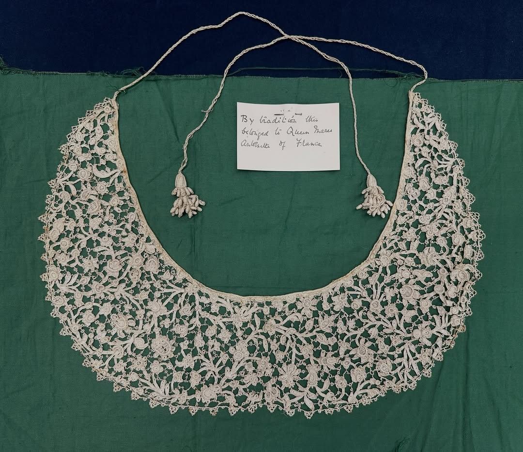 A white lace collar with tassels laid on a green cloth with a handwritten label.